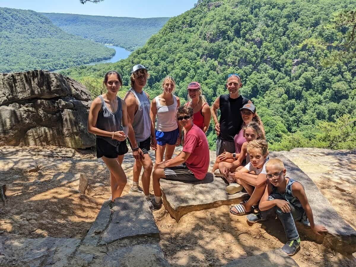 A group of people on a rocky outcrop with a river and forested hills in the background.