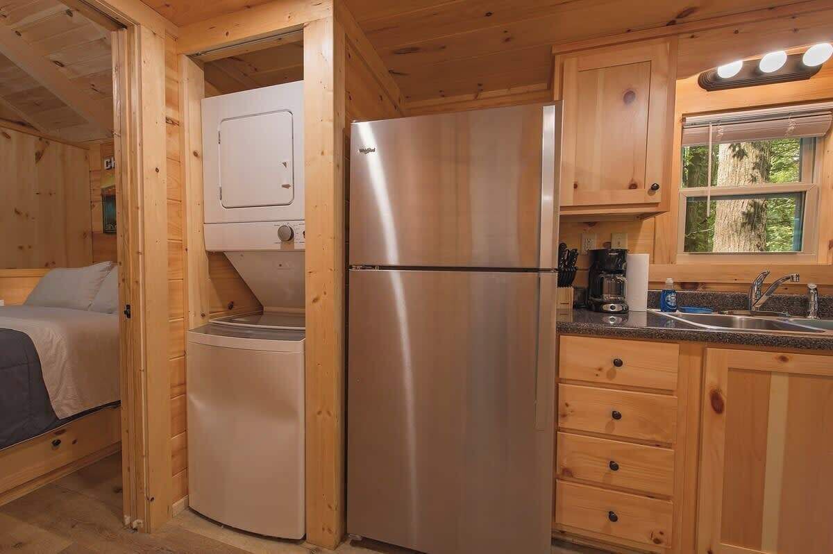 Ein gemütliches Holzhaus mit einer Küchenzeile, einem Bett und einem Fenster mit Blick auf Bäume.