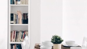 Una estanteria plena de llibres, una petita planta en test i bols blancs sobre una taula.
