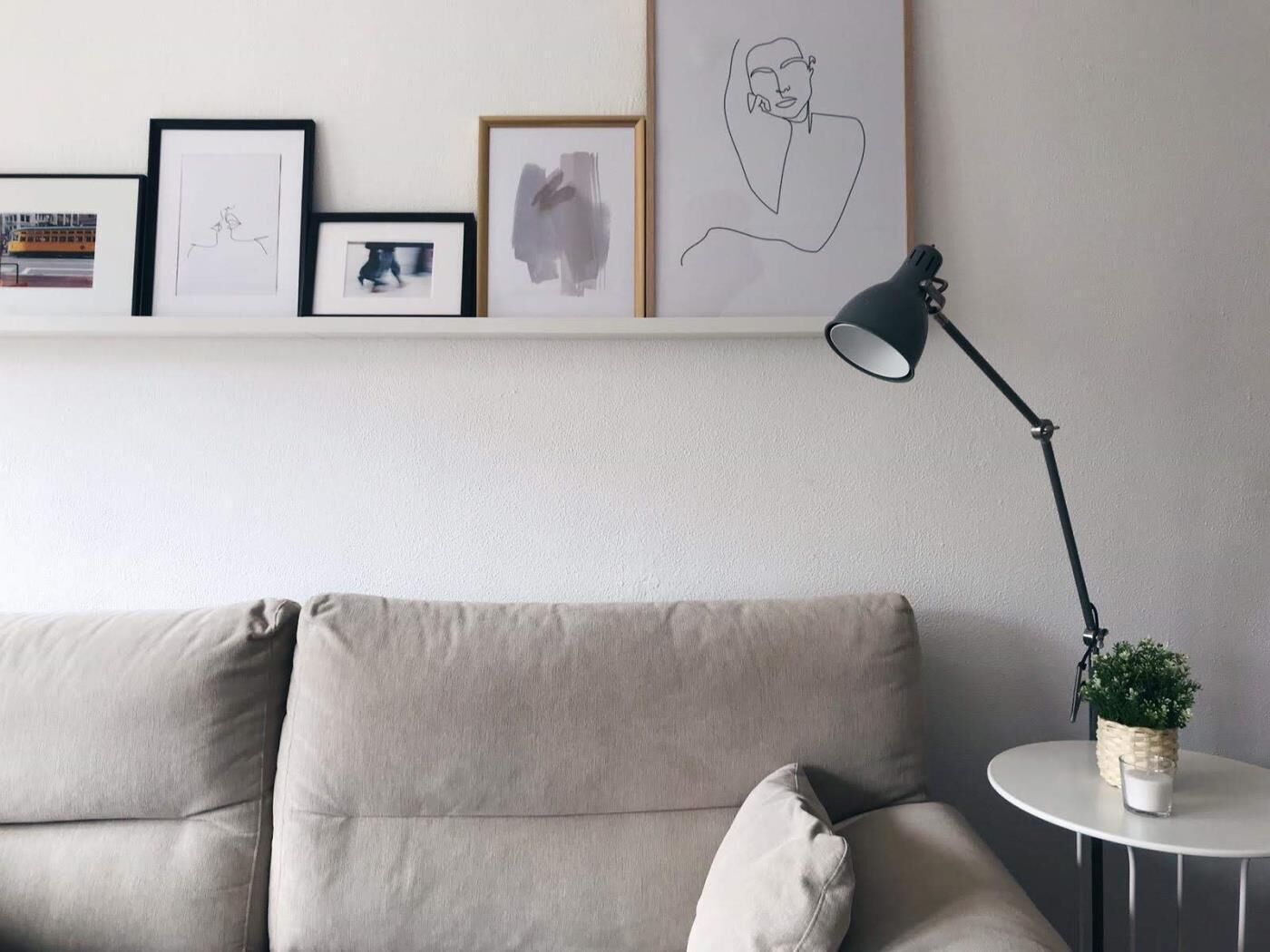En moderne stue med en grå sofa, et lille rundt bord med en plante og et lys, og en væg med indrammede kunstværker.