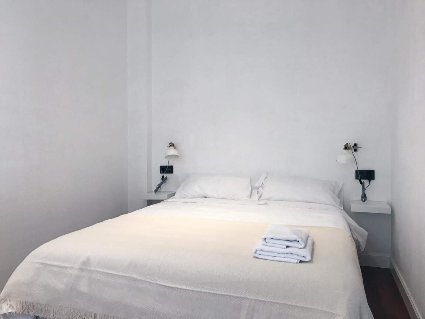 Een strakke hotelkamer met een groot bed, witte lakens en twee nachtkastjes met lampen.