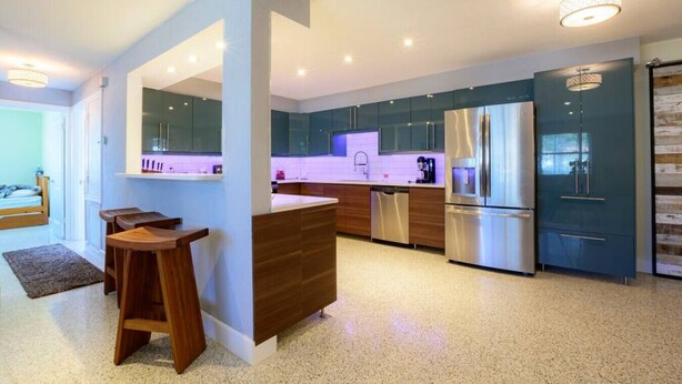 A modern kitchen with stainless steel appliances, a central island, and a dining area with wooden stools.