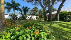 A well-maintained garden with a variety of plants and trees, a clear sky, and a building with a metal roof in the background.