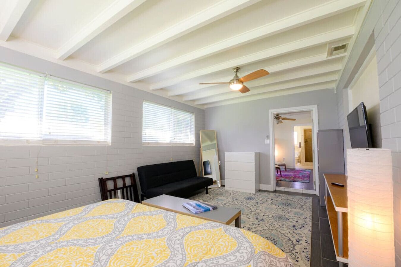 Una habitación con cama, sofá, escritorio, ventilador de techo y puerta que da a otra estancia.