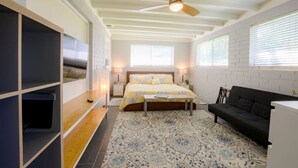 A bedroom with a bed, a desk, a black sofa, a ceiling fan, and a patterned rug.