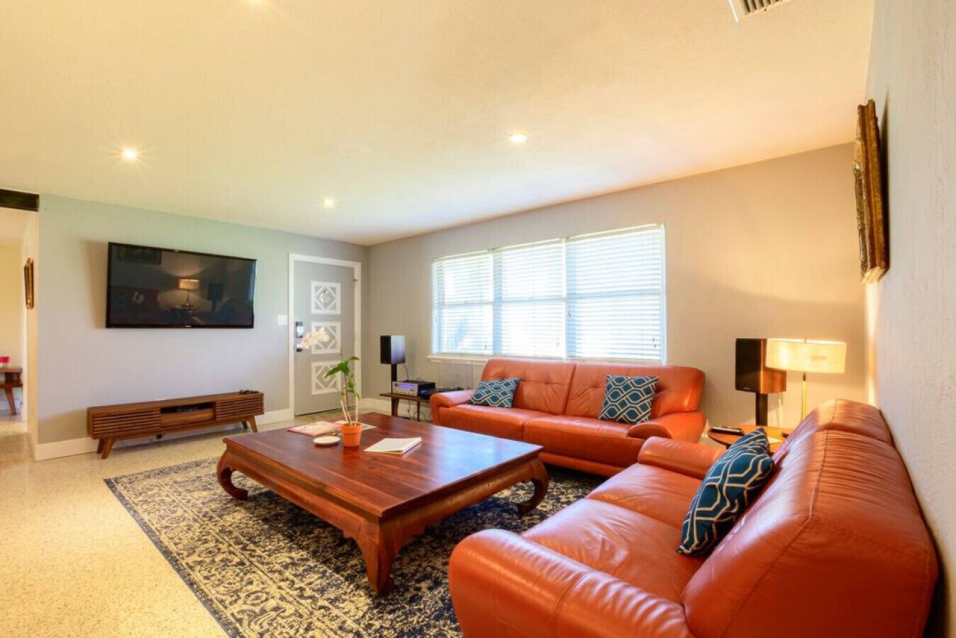Una sala de estar con un conjunto de sofá, una mesa de centro, un televisor y una ventana con persianas.