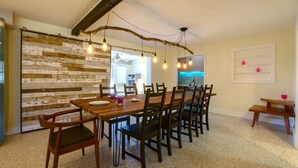 A dining area with a rustic wooden wall, a wooden dining table with chairs, and pendant lights.