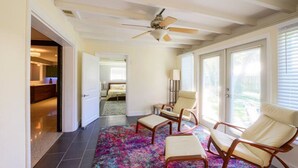 A spacious living area with a ceiling fan, a colorful rug, and a seating area with two chairs and a small table.