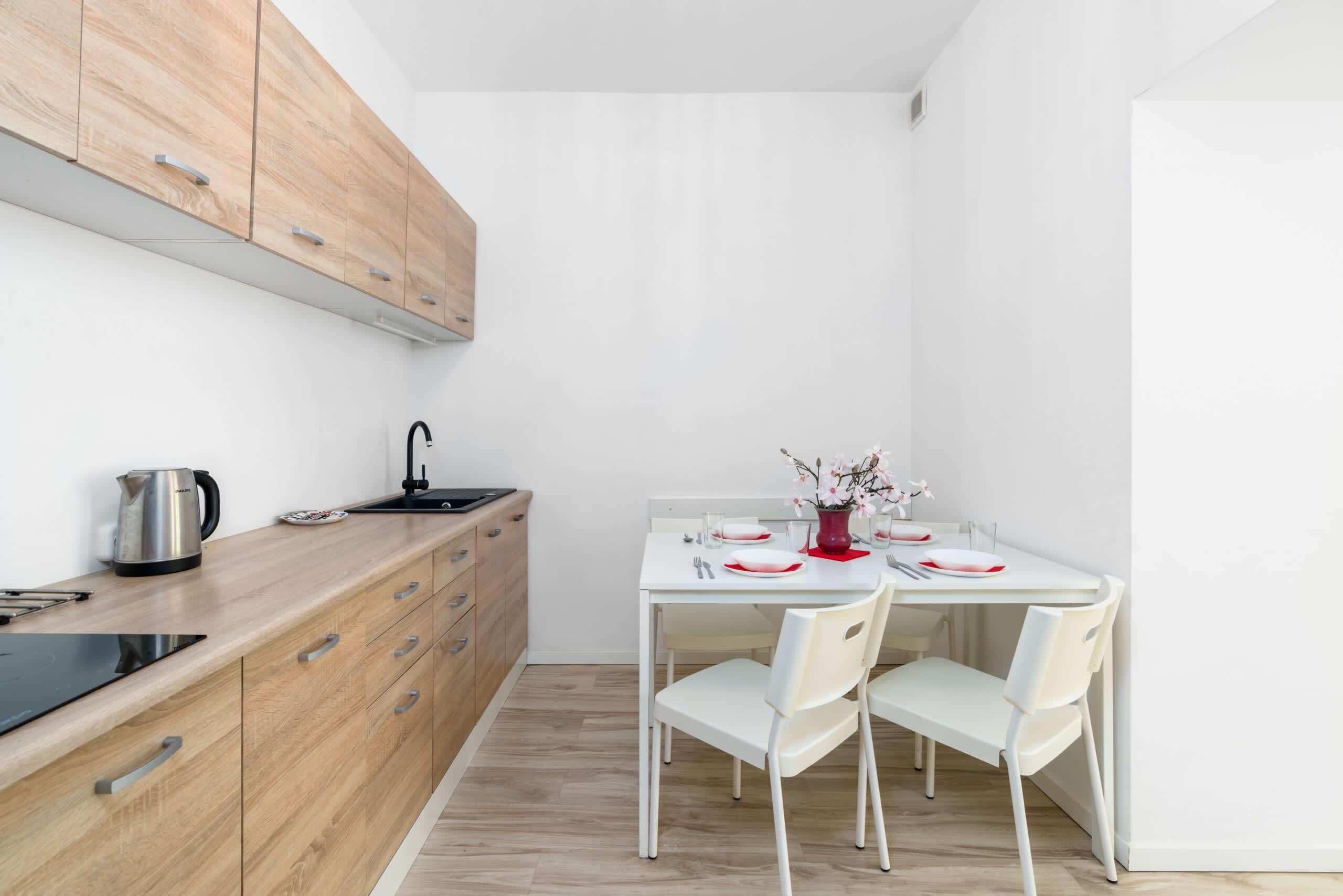 A compact kitchen with wooden cabinets, a white countertop, and a dining area with a white table and chairs.