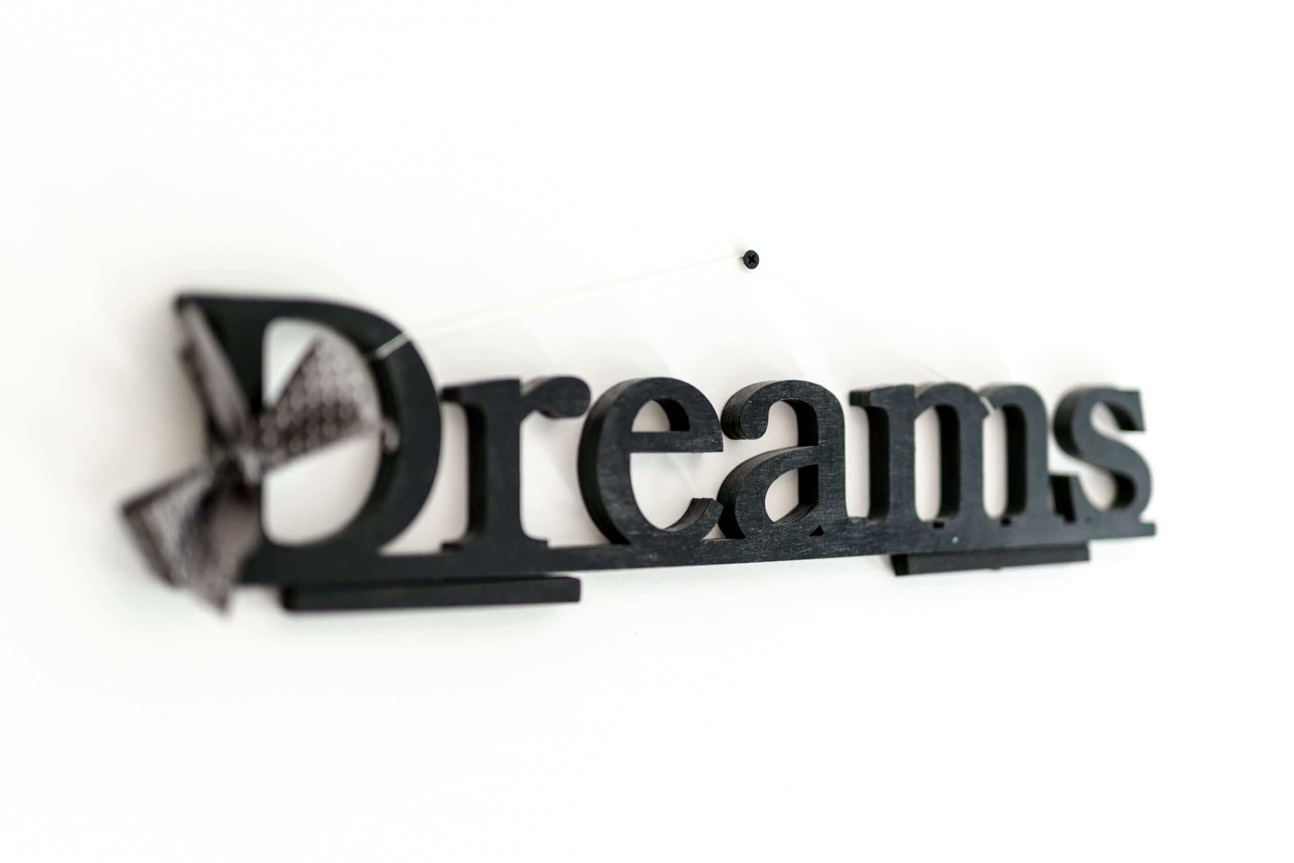 Un panneau noir sur lequel est inscrit le mot « Dreams » dans une police de caractères stylisée.