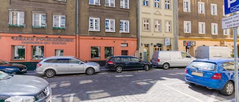 A street view with parked cars, a building with a sign reading "USEGUI POGRZEBOWE DOBROWOLSKI-HIERNES", and a blue parking sign.