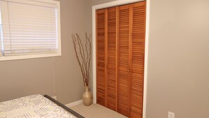 Un dormitorio con cama, ventana con persianas, armario de madera y un jarrón con ramas.