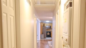 Un pasillo con piso de madera, paredes blancas y una puerta blanca a la izquierda.