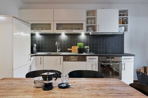 A modern kitchen with white cabinets, a black countertop, and a wooden dining table.