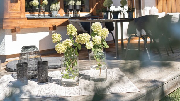 A wooden deck with a table, chairs, and potted plants.