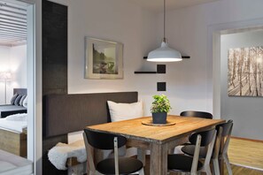 A modern room with a wooden dining table, black chairs, a hanging pendant light, a grey sofa, a white pillow, a framed picture, and a potted plant.
