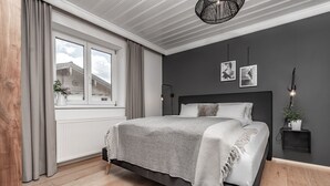 A bedroom with a bed, a window, a radiator, a plant, and a wall-mounted light fixture.