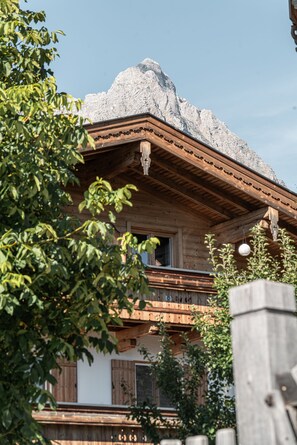 A wooden chalet with a stone roof, wooden balcony, and a wooden fence in the foreground.