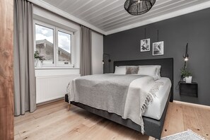 A bedroom with a bed, a window, a radiator, a plant, and a wall-mounted light fixture.