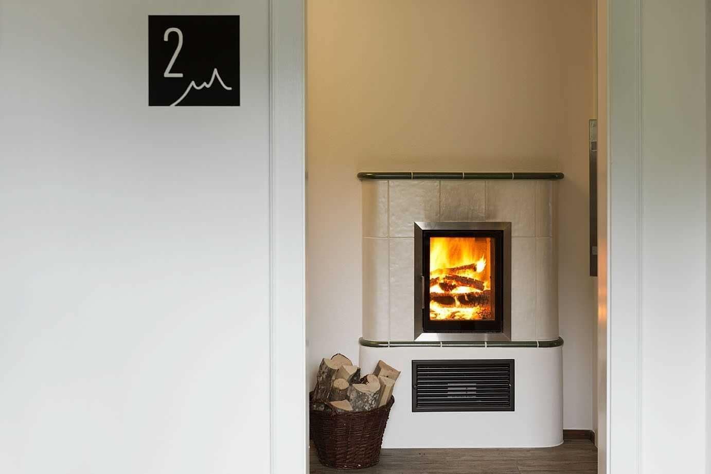 Ein moderner Kamin mit sichtbarem Feuer, einem Hinweisschild und einem Holzkorb.