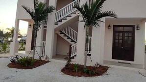 Un edificio di due piani con una scala, un'entrata scura e due palme sullo sfondo.