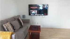 Un soggiorno con un divano grigio, un tavolino in legno e una TV a schermo piatto montata a parete che mostra la serie Netflix "The Equalizer".
