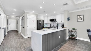 A modern kitchen with a central island, white cabinetry, and a grey floor. - Centre Ridge Escape | 3BR Modern Condo w/ Golf Course Views in Reunion Resort Near Disney (Kissimmee)