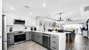 A modern kitchen with stainless steel appliances, a central island, and a dining area with a view. - Centre Ridge Escape | 3BR Modern Condo w/ Golf Course Views in Reunion Resort Near Disney (Kissimmee)