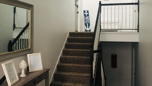 Un escalier recouvert d’une moquette sombre mène au deuxième étage. Une balustrade blanche se trouve sur le palier supérieur.