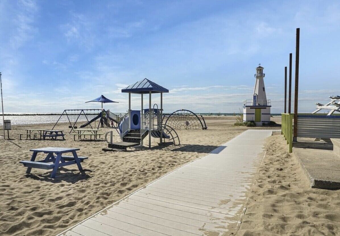 Une plage avec une promenade en bois, une aire de jeux, une table de pique-nique et un phare en arrière-plan.