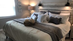 Un lit bien fait, aux couleurs gris et blanc, avec une lampe de chevet et un élément décoratif mural.