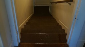 Eine Treppe mit Holzbalken und Geländer, die zu einer Zwischenebene führt, auf der ein gerahmtes Bild an der Wand hängt.