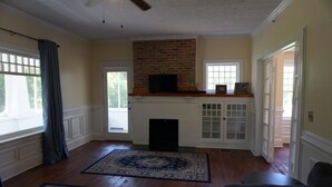 Ein Wohnzimmer mit Holzdielenboden, einem Kamin mit Ziegelverkleidung, einem Fernseher auf dem Sims und einem großen Teppich.