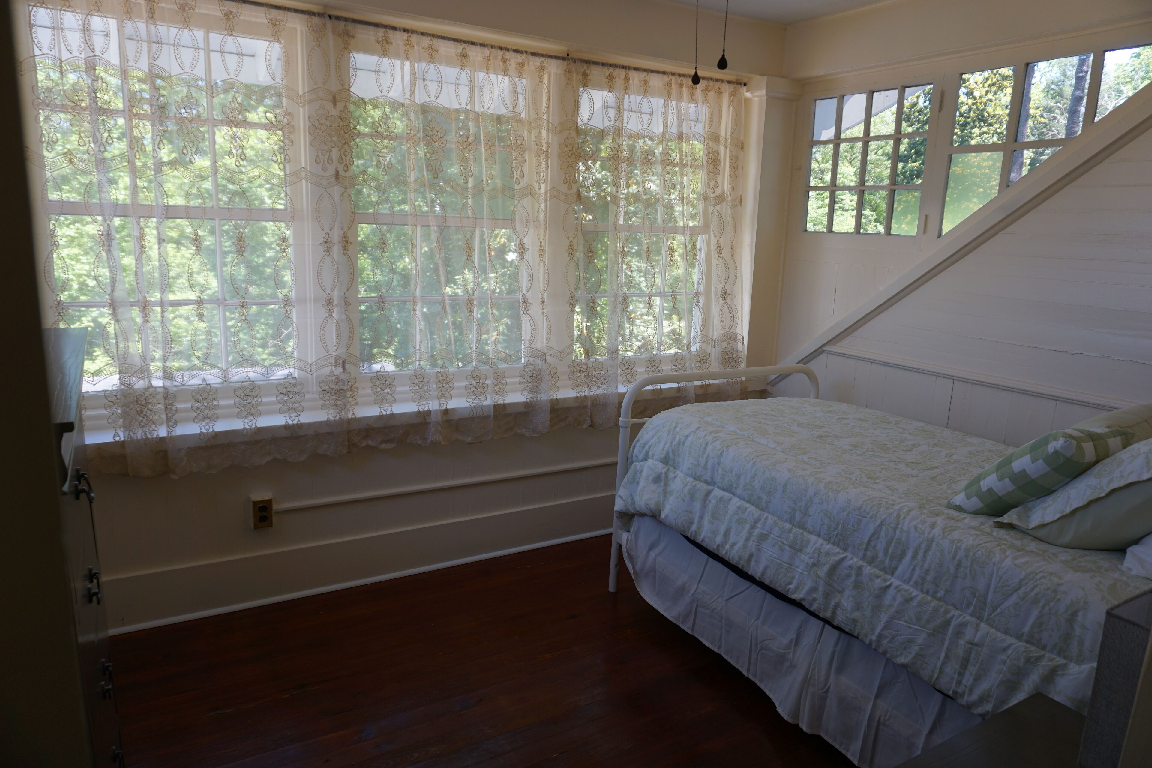 A bedroom with a bed, a window with curtains, and a view of trees.