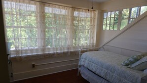 Ein Schlafzimmer mit Bett, einem Fenster mit Vorhängen und Blick auf Bäume.