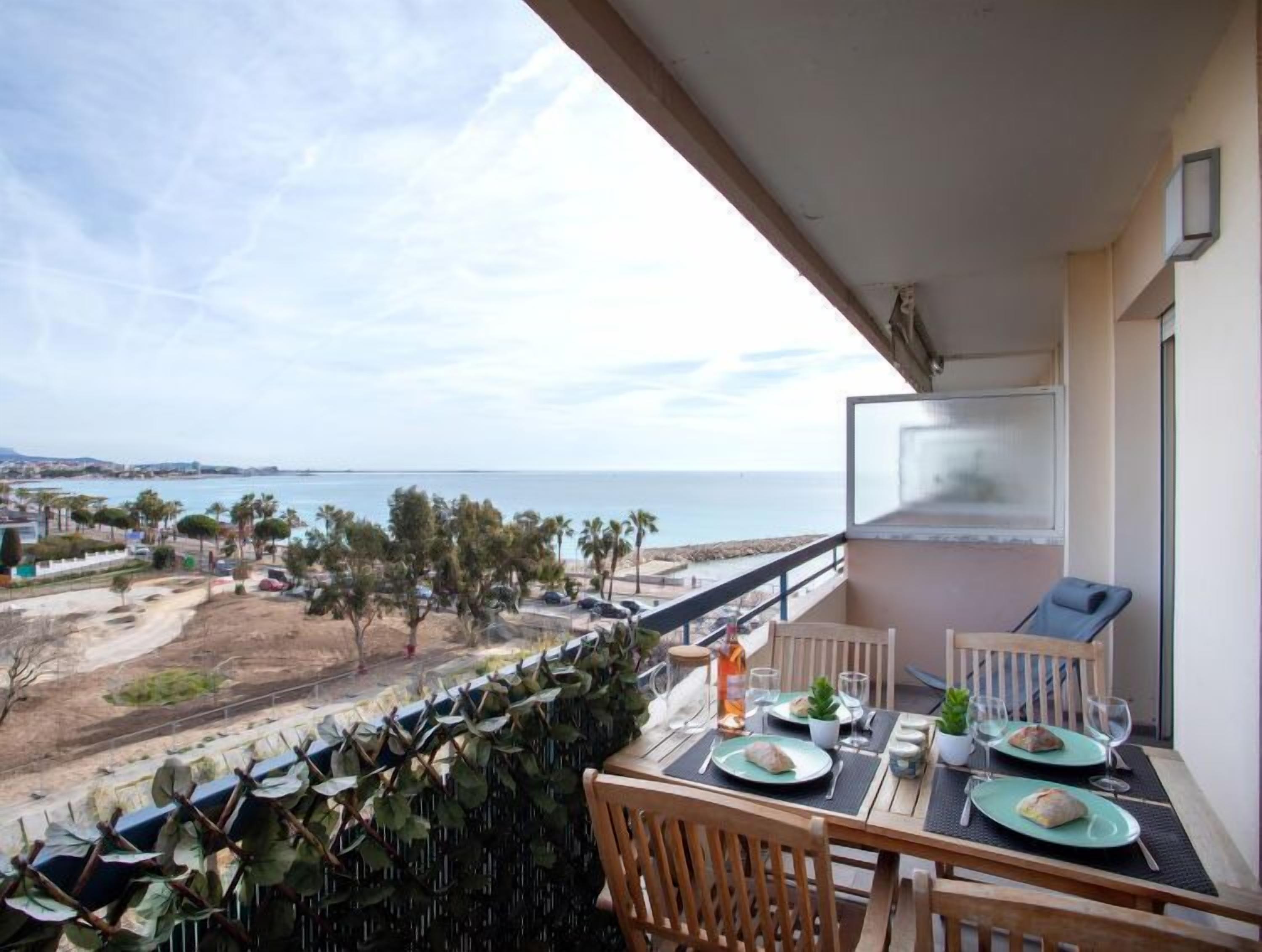 Ein Balkon mit Tisch für zwei Personen, mit Blick auf einen Strand und eine Küstenstraße.