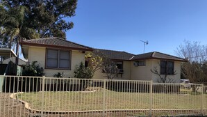 Ein Wohnhaus mit umzäuntem Garten, einer sichtbaren Satellitenschüssel und einem kleinen Baum davor.