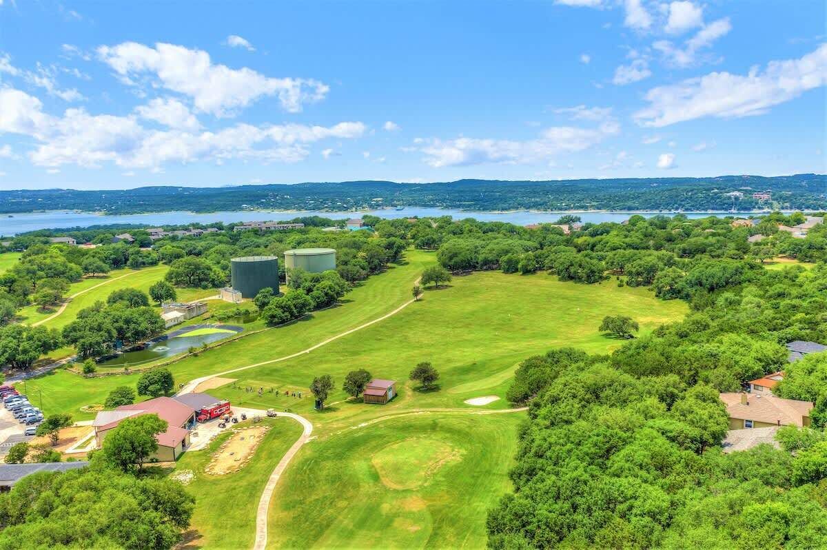 An aerial view of a golf course with a lake in the background, surrounded by trees and residential areas.