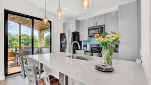 Une cuisine moderne dotée d’un grand îlot central, d’appareils électroménagers en acier inoxydable et donnant sur une terrasse extérieure.