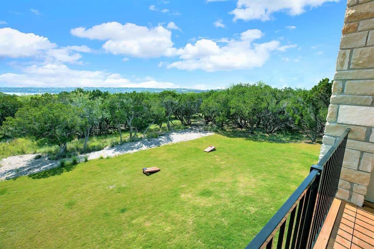 A balcony with a stone wall and a view of a grassy yard with trees and a distant landscape.