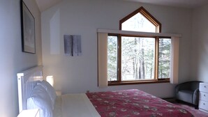 Een slaapkamer met een bed, een raam met uitzicht op bomen, een dressoir en een ingelijst schilderij aan de muur.
