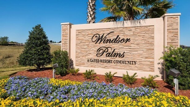 En skylt för Windsor Palms, ett exklusivt bostadsområde med bevakad entré, med en fasad av sten och en vacker trädgård med blommor runt omkring.