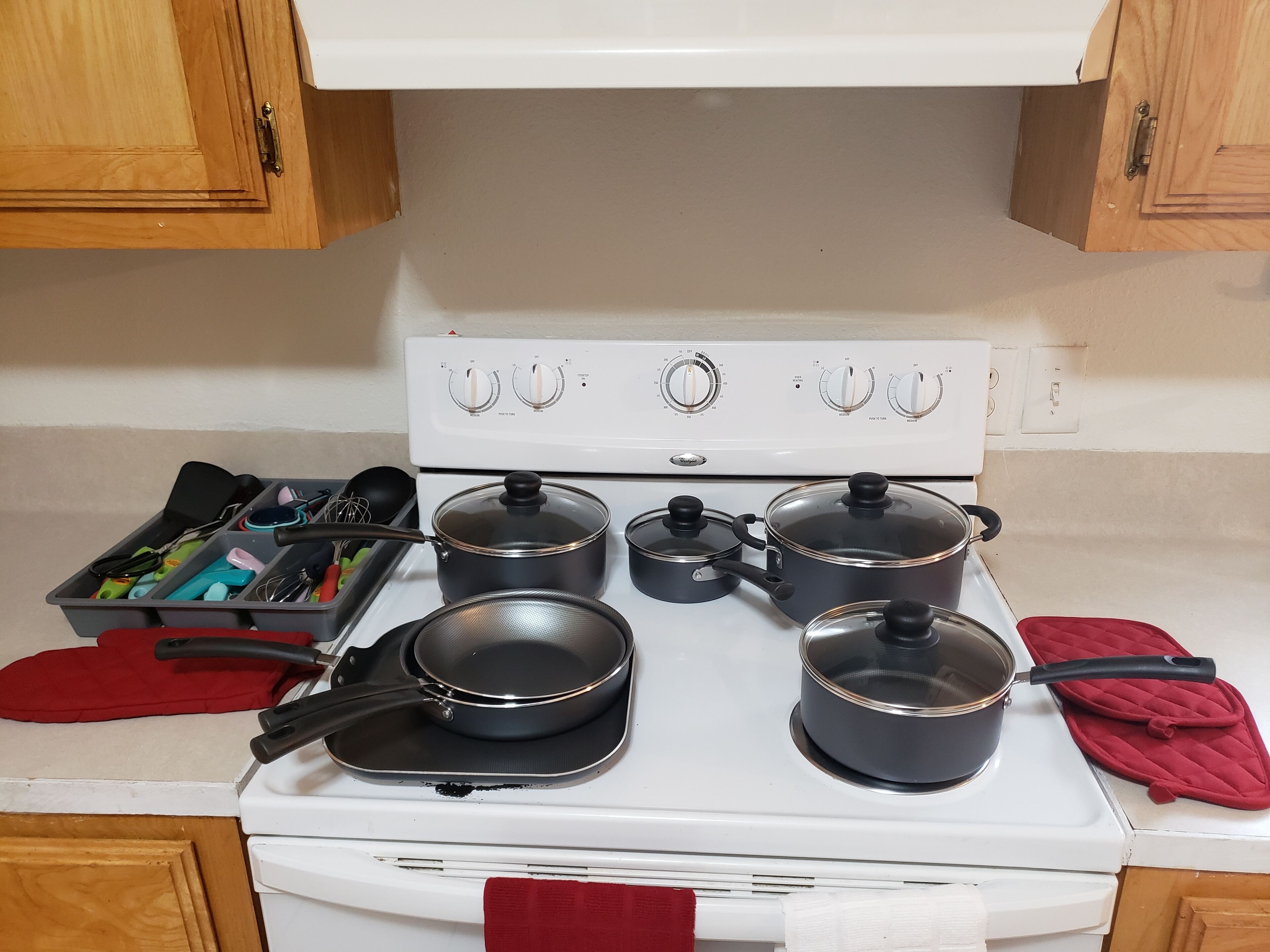 Une cuisine avec un four blanc, quatre casseroles, une poêle et divers ustensiles.
