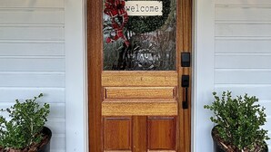 A wooden front door with a glass panel, a welcome sign, and two potted plants on either side. - Renovated Cottage - Walk to Downtown Mentone (Mentone)