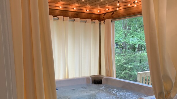 A wooden hot tub with a view of a forest, surrounded by curtains and string lights. - Renovated Cottage - Walk to Downtown Mentone (Mentone)