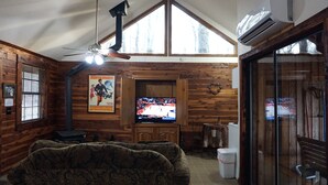 A wooden-paneled room with a ceiling fan, a television displaying a sports event, and a large window. - Couples Getaway Near Hot Springs-Jacuzzi and Hot Tub Overlooking Mountains! (Bismarck)