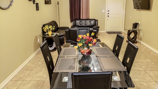 Un coin repas avec une table à plateau en verre, des chaises noires, un vase de fleurs et un canapé en cuir noir.