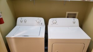 Deux machines à laver à chargement frontal, de couleur blanche, se trouvent dans une buanderie aux murs de couleur beige et dotée d’une petite fenêtre.