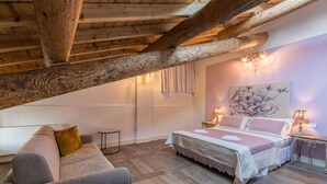 A bedroom with a wooden ceiling, a bed, a sofa, a small table, and a wall with a floral painting. - Apartment "Ontano" in Agriturismo Style with Wi-Fi, Garden, and Shared Pool (Desenzano)