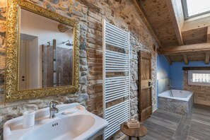 A bathroom with a stone wall, a large mirror, a sink, a bathtub, and a window.